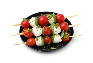 Plate of Caprese skewers with tomatoes, mozzarella balls, basil and pesto sauce isolated on white