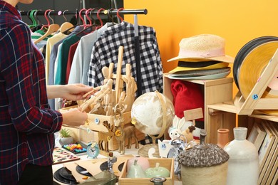 Photo of Woman holding wooden figure near table with different stuff indoors, closeup. Garage sale