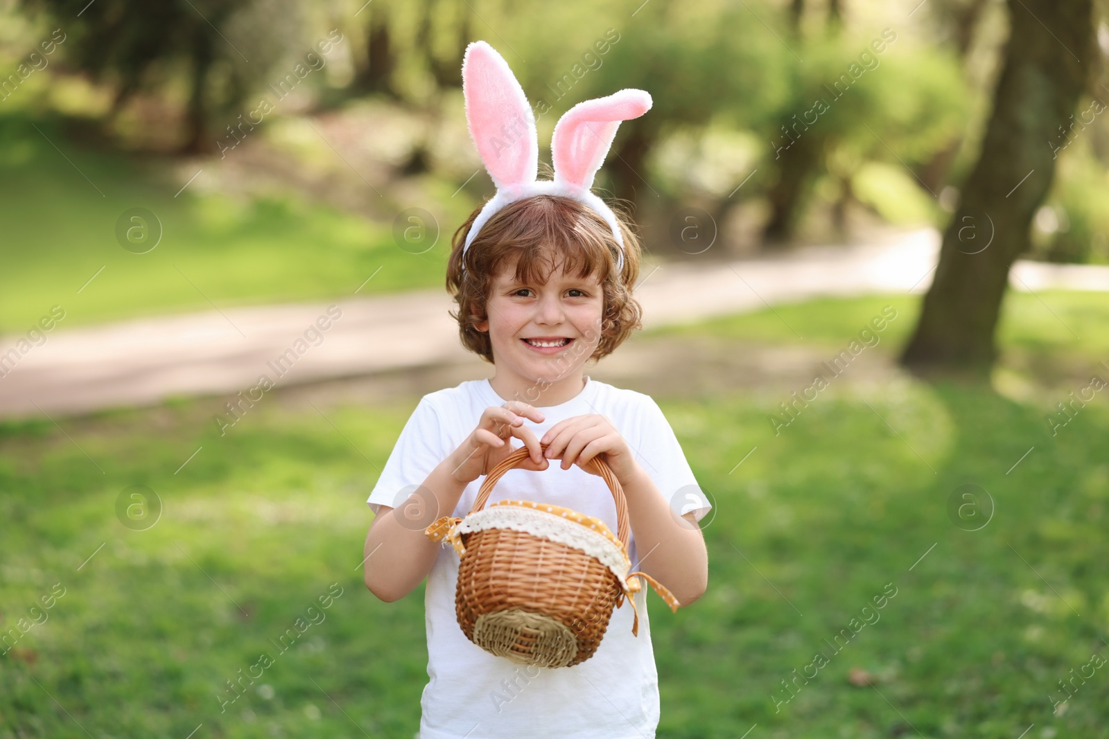 Photo of Easter celebration. Cute little boy in bunny ears holding wicker basket outdoors