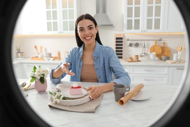 Blogger with cake recording video in kitchen at home, view through ring lamp