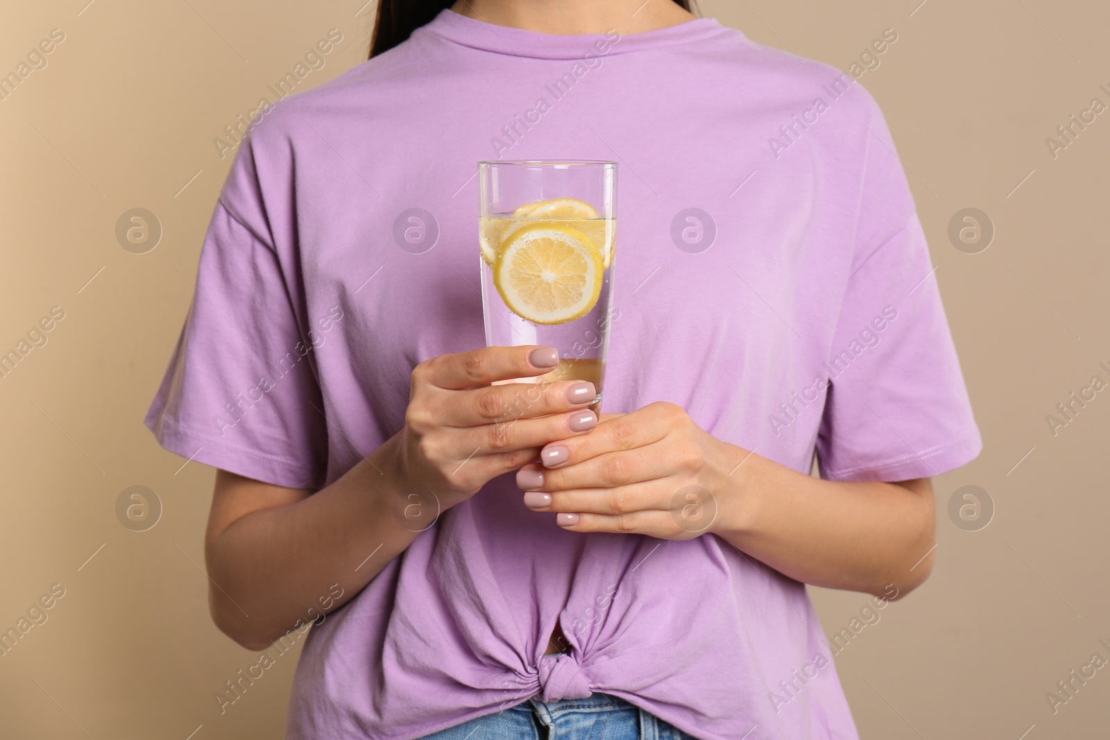 Photo of Woman with tasty lemon water on beige background, closeup