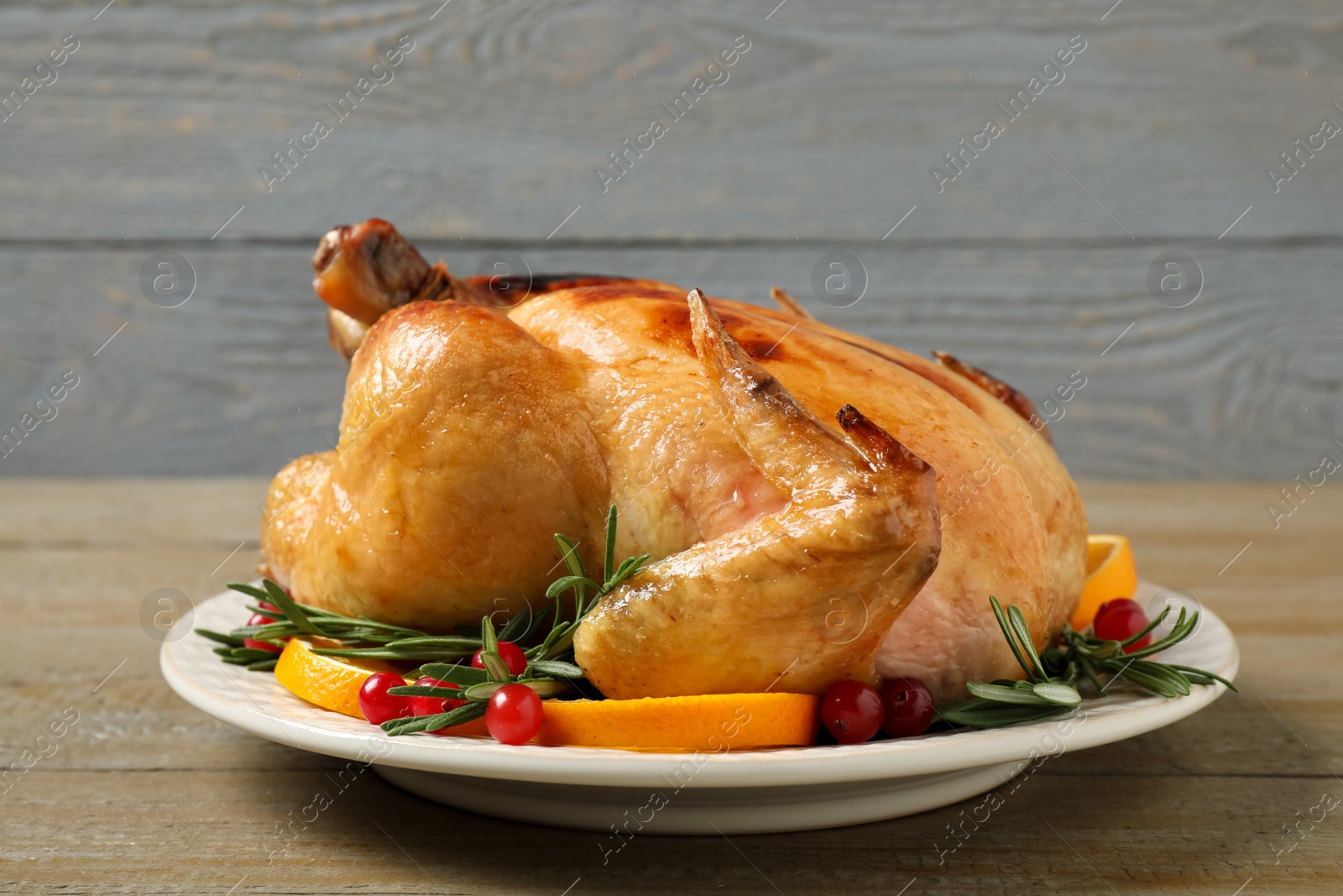 Photo of Delicious cooked turkey served with rosemary, oranges and cranberries on wooden table. Thanksgiving Day celebration