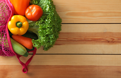 Net bag with vegetables on wooden table, top view. Space for text