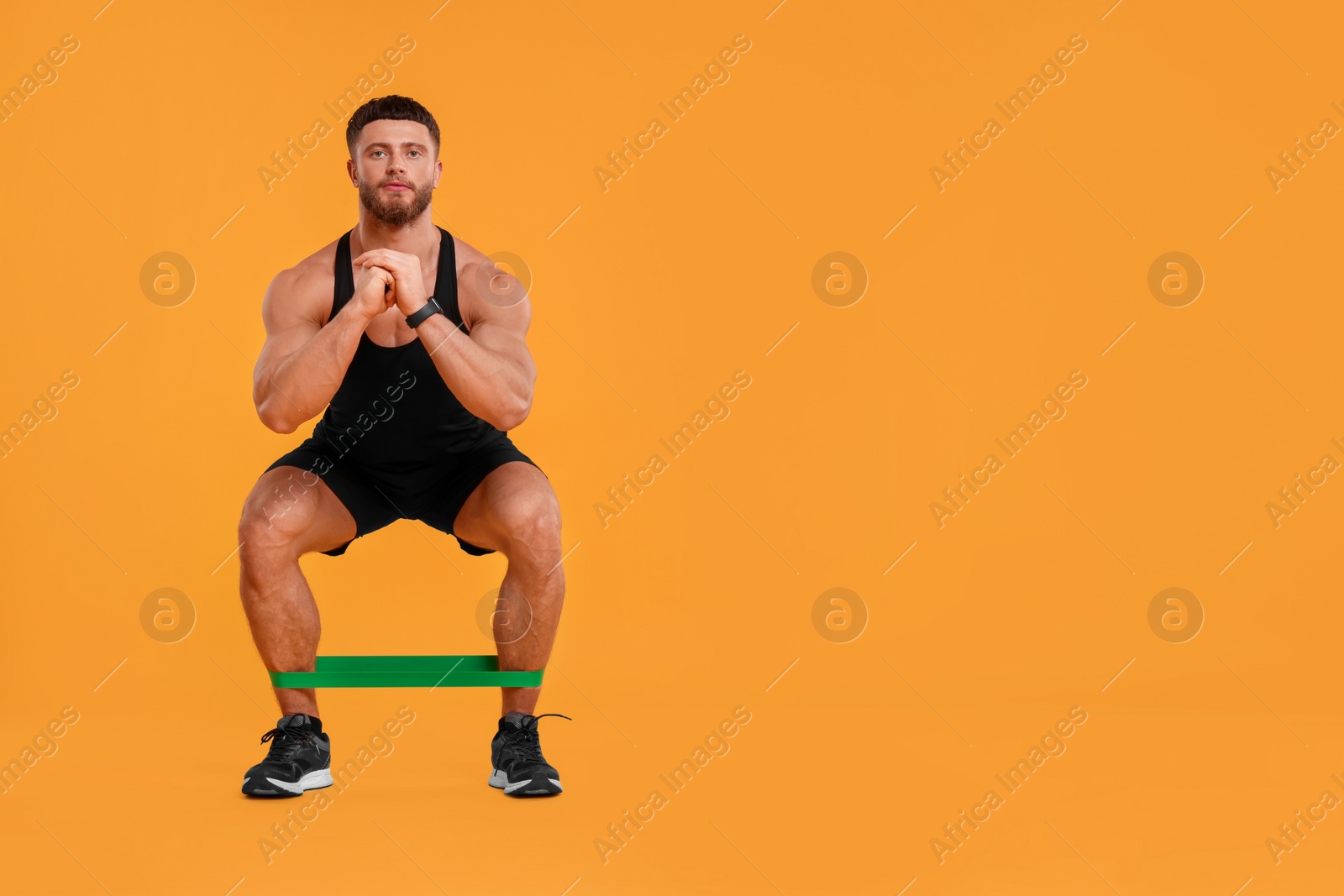 Photo of Young man exercising with elastic resistance band on orange background. Space for text