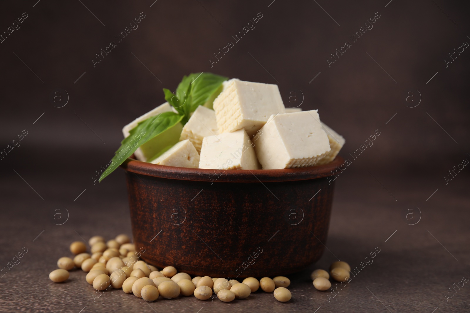 Photo of Delicious tofu cheese, basil and soybeans on brown textured table, closeup
