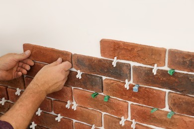Photo of Professional builder installing new brown decorative bricks on wall, closeup