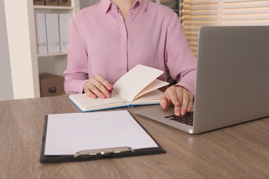 Photo of Woman taking notes while using laptop at wooden table indoors, closeup