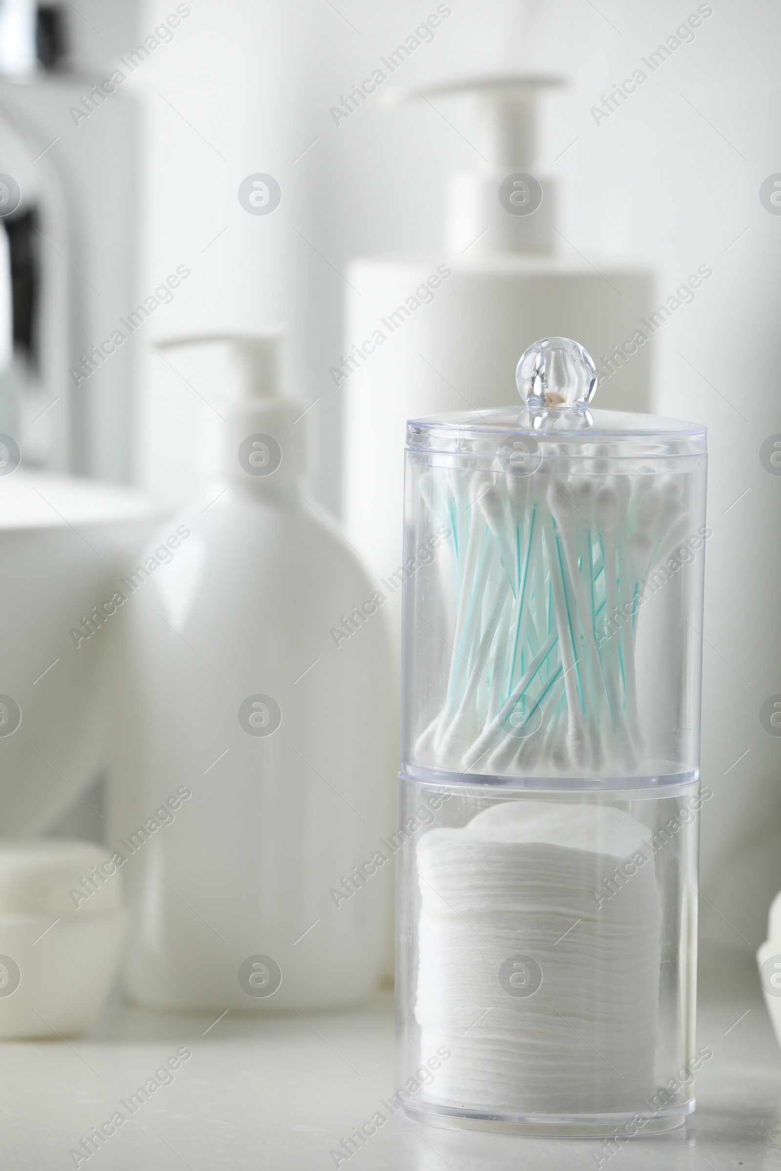 Photo of Containers with cotton swabs and pads near cosmetic products on white countertop in bathroom