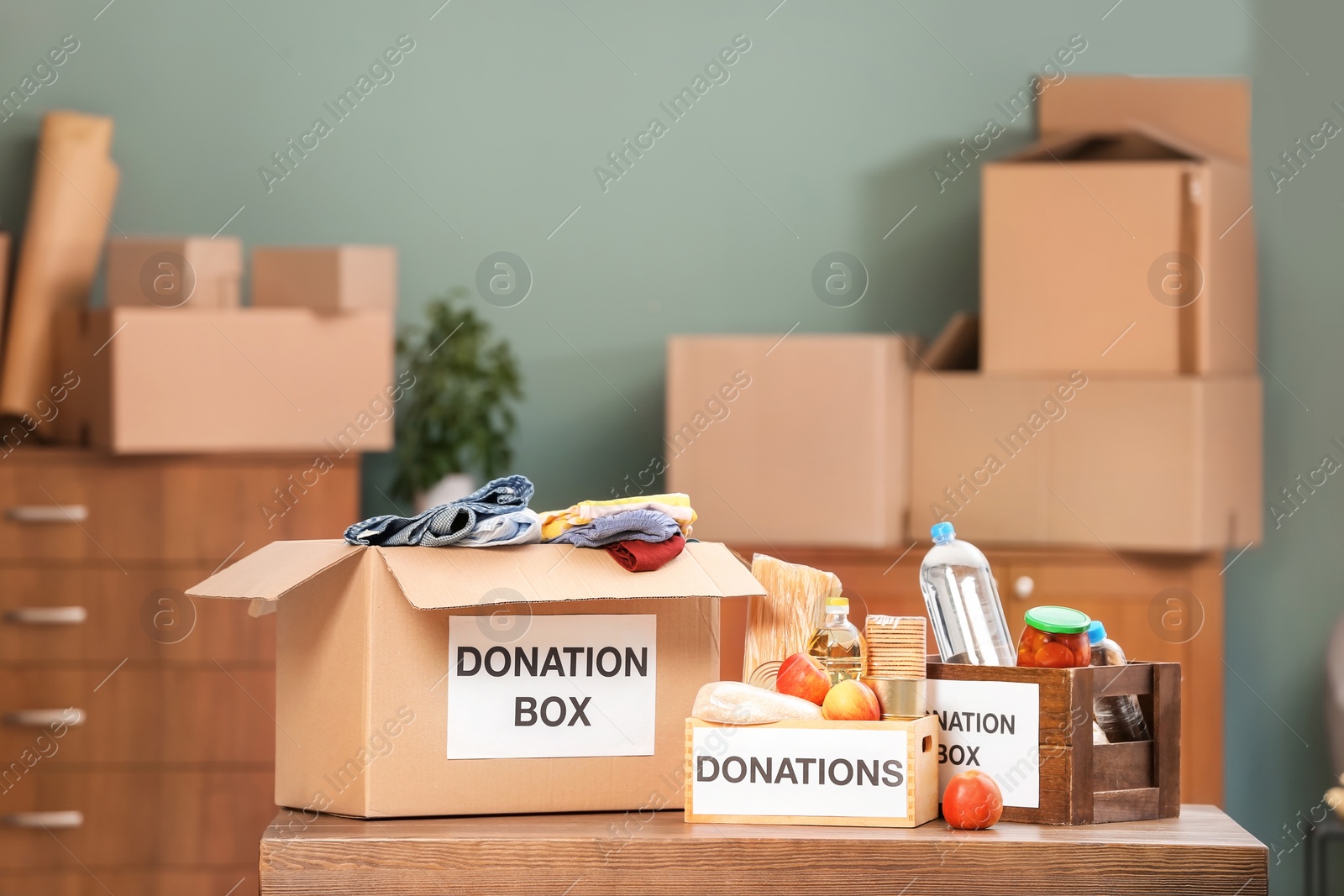 Photo of Donation boxes with food products and clothes on table indoors