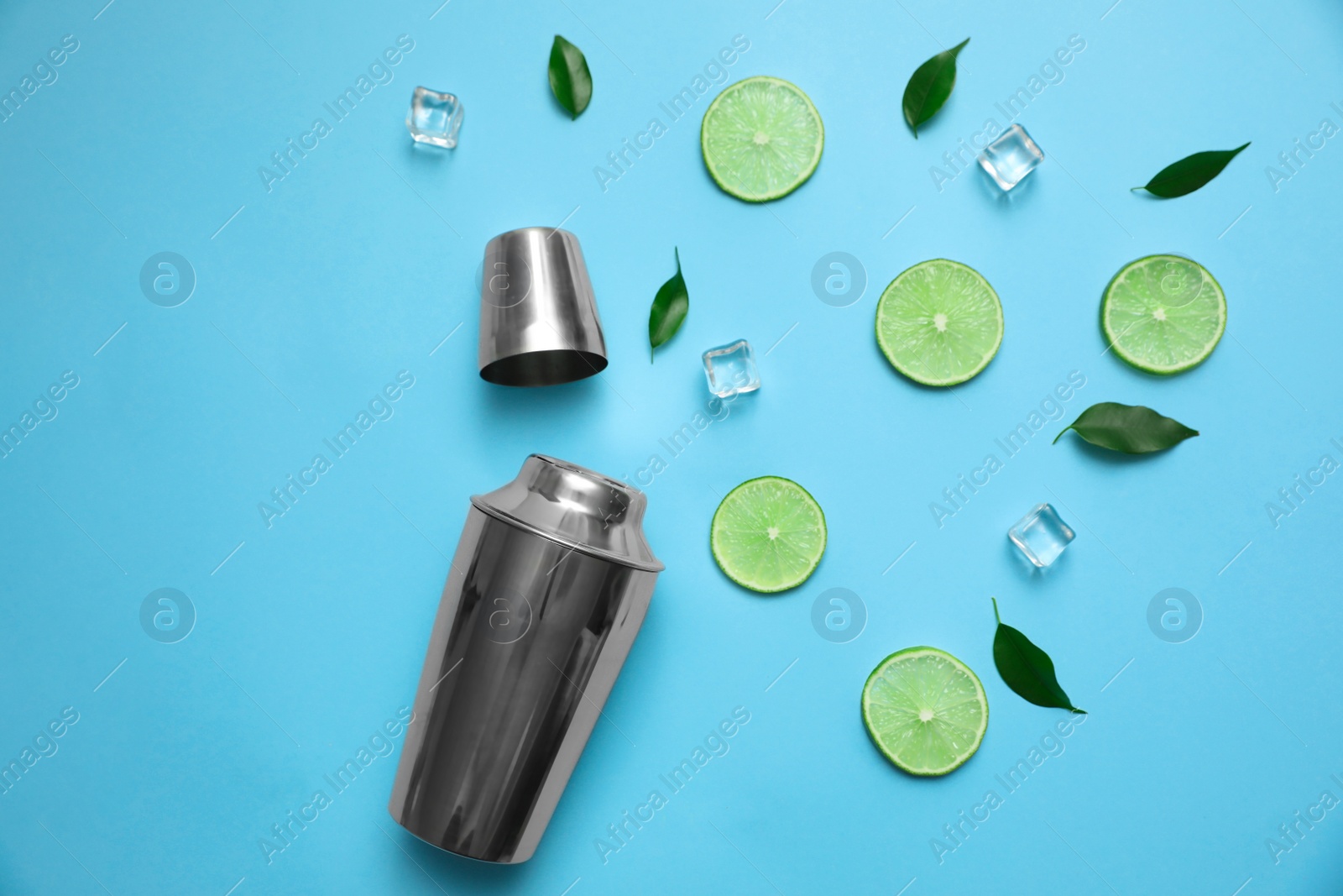 Photo of Flat lay composition with fresh juicy limes, ice cubes and cocktail shaker on light blue background