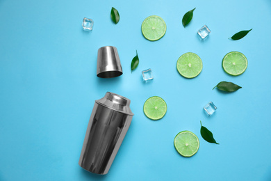 Photo of Flat lay composition with fresh juicy limes, ice cubes and cocktail shaker on light blue background