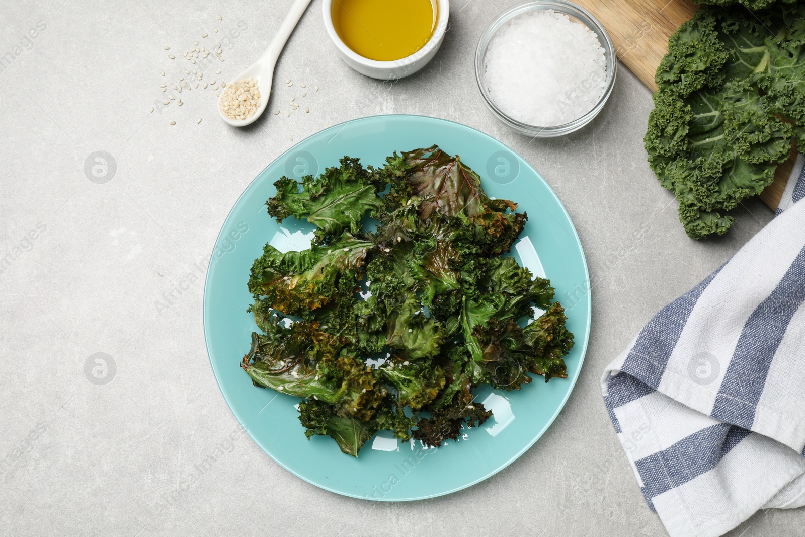 Photo of Tasty baked kale chips on light grey table, flat lay