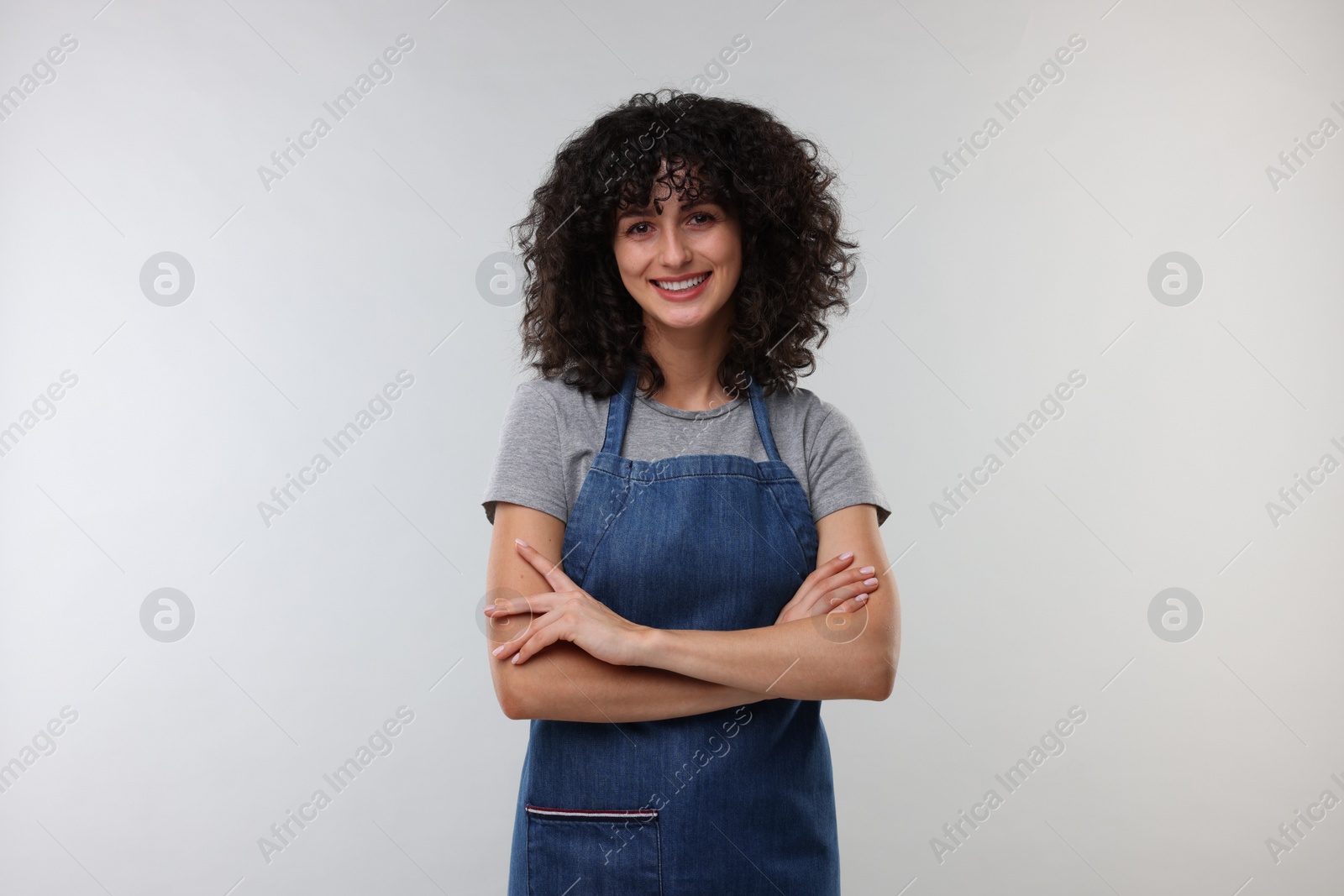 Photo of Happy woman wearing kitchen apron on light grey background. Mockup for design