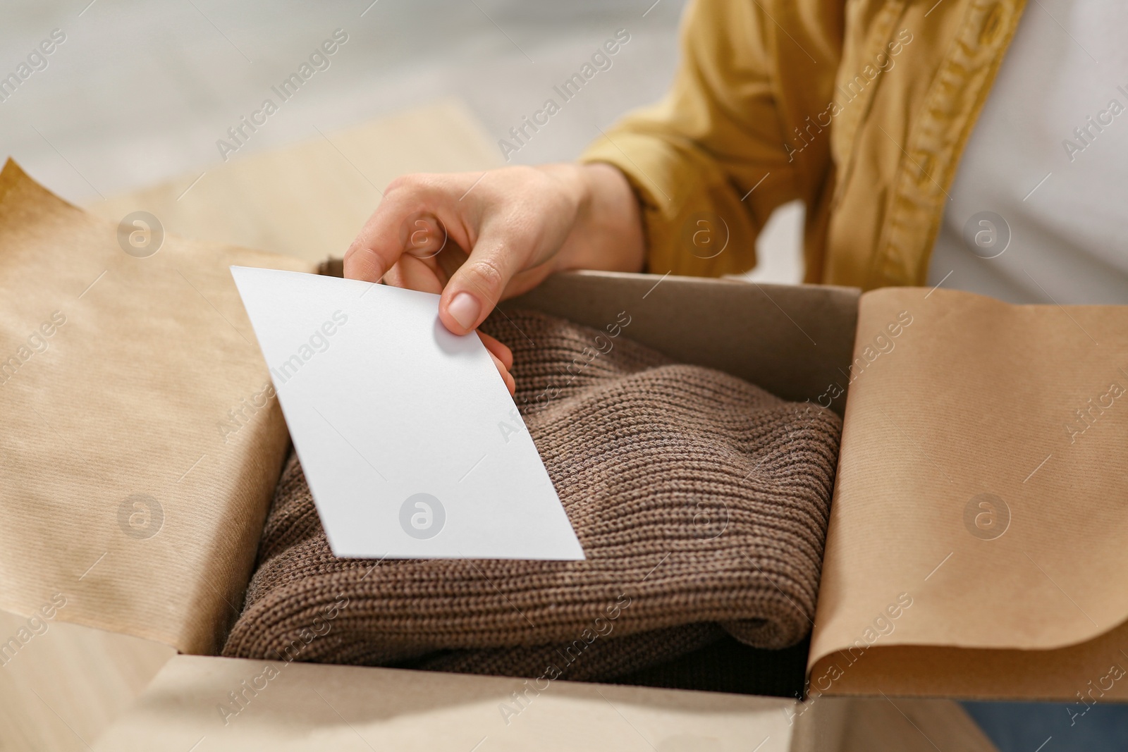 Photo of Woman holding greeting card near parcel with Christmas gift indoors, closeup