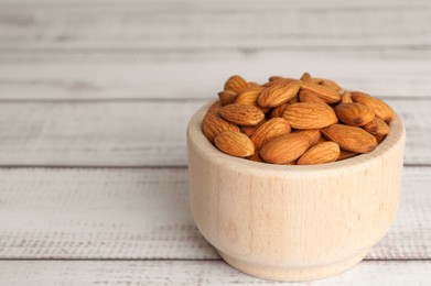Tasty almonds in bowl on wooden table, space for text