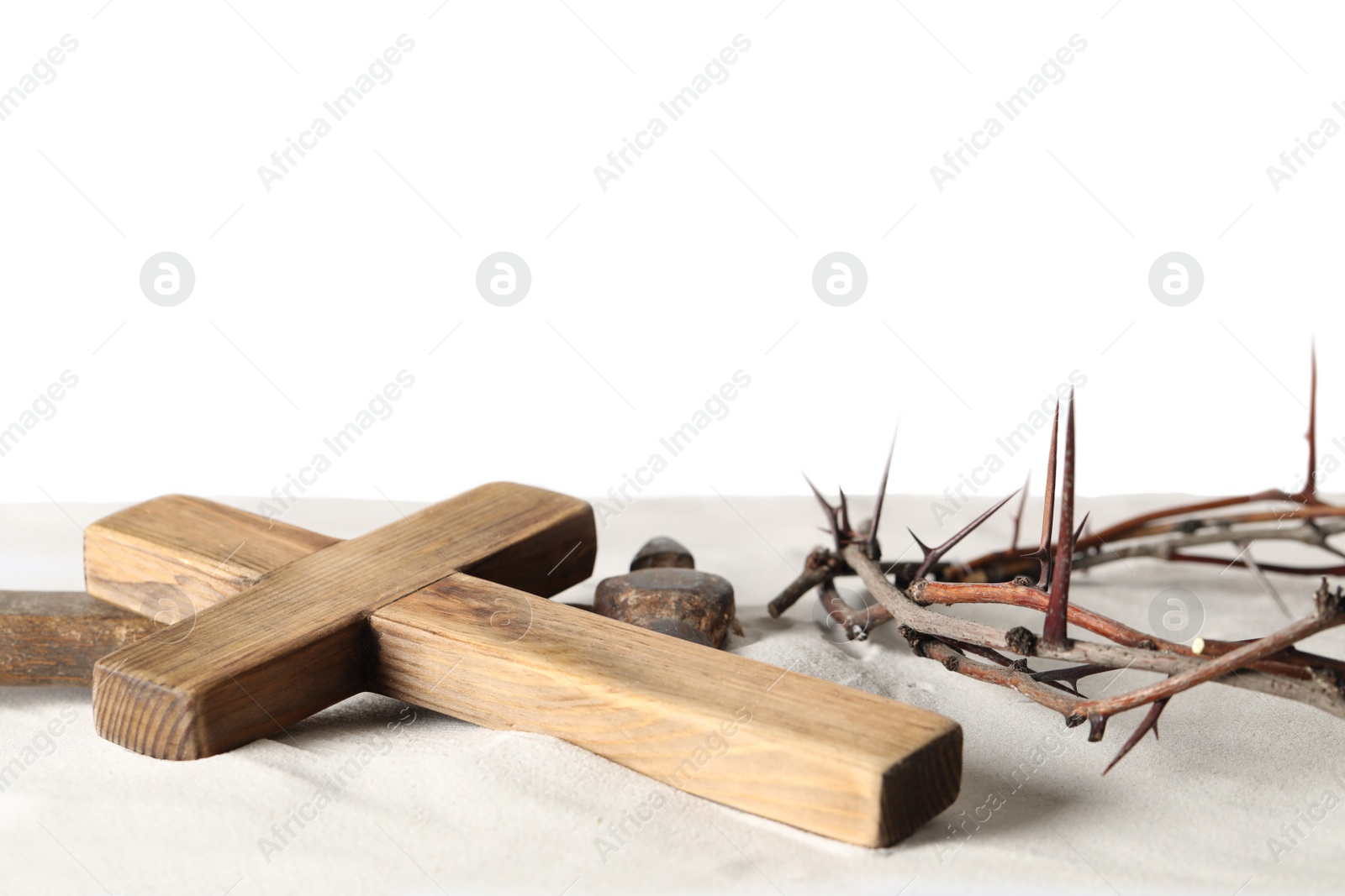 Photo of Crown of thorns, wooden cross and hammer on sand against white background, space for text. Easter attributes