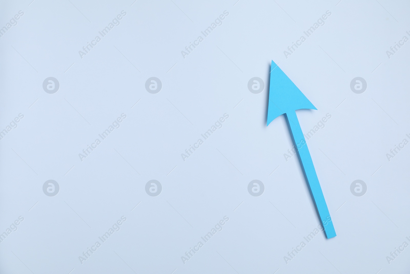 Photo of Light blue paper arrow on white background, top view. Space for text