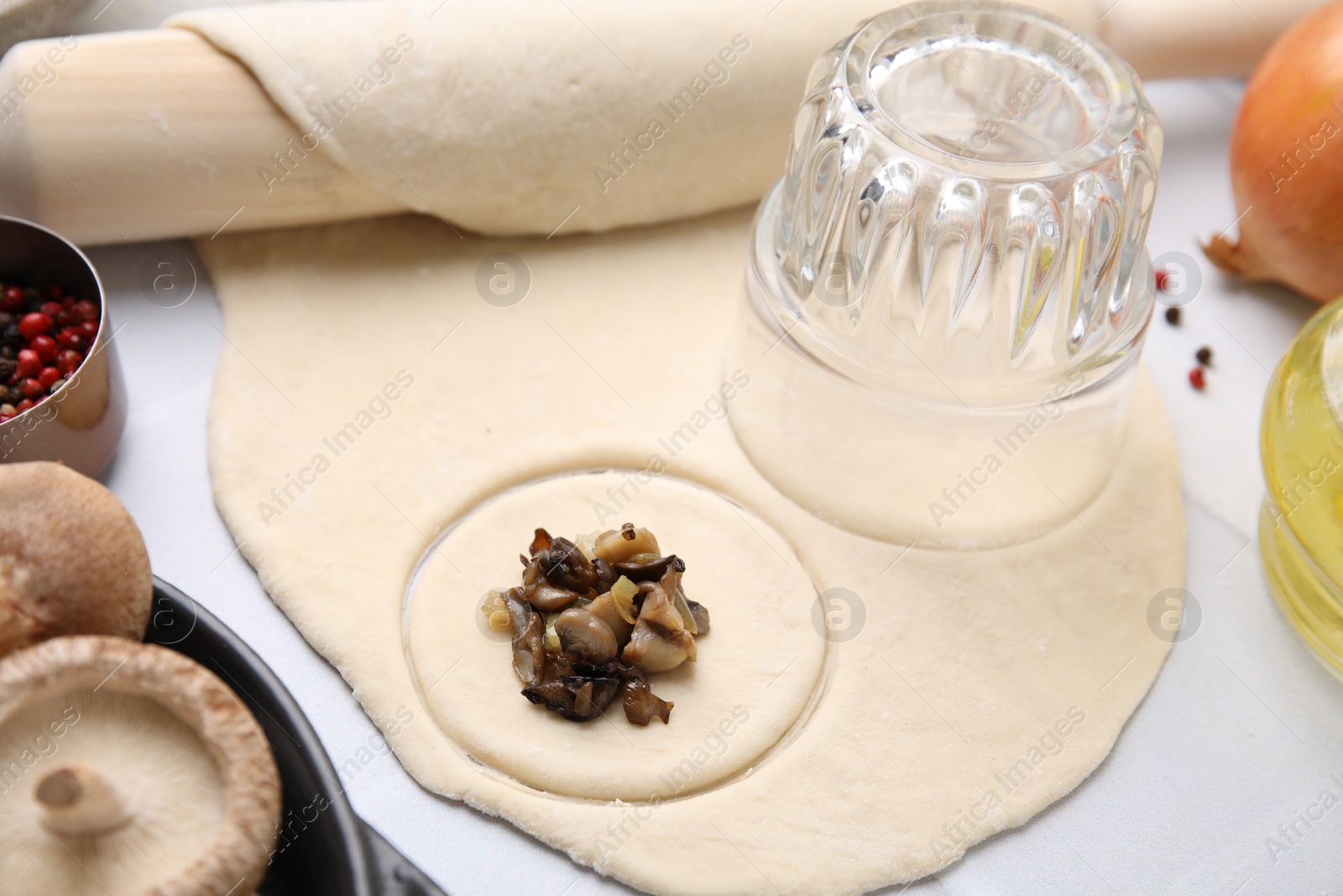 Photo of Process of making dumplings (varenyky) with mushrooms. Raw dough and ingredients on white table, closeup