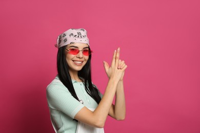 Young woman wearing stylish bandana and sunglasses on pink background, space for text