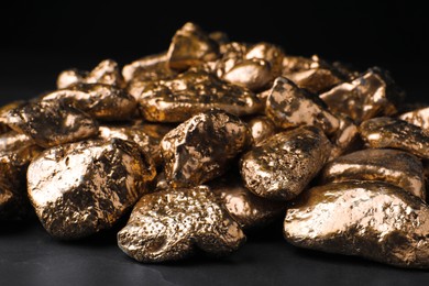 Photo of Pile of gold nuggets on black table against dark background, closeup