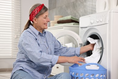 Happy housewife putting laundry into washing machine at home