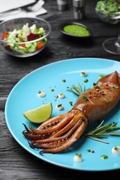 Delicious grilled squid served on black wooden table, closeup