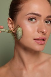Photo of Young woman massaging her face with jade roller on green background, closeup