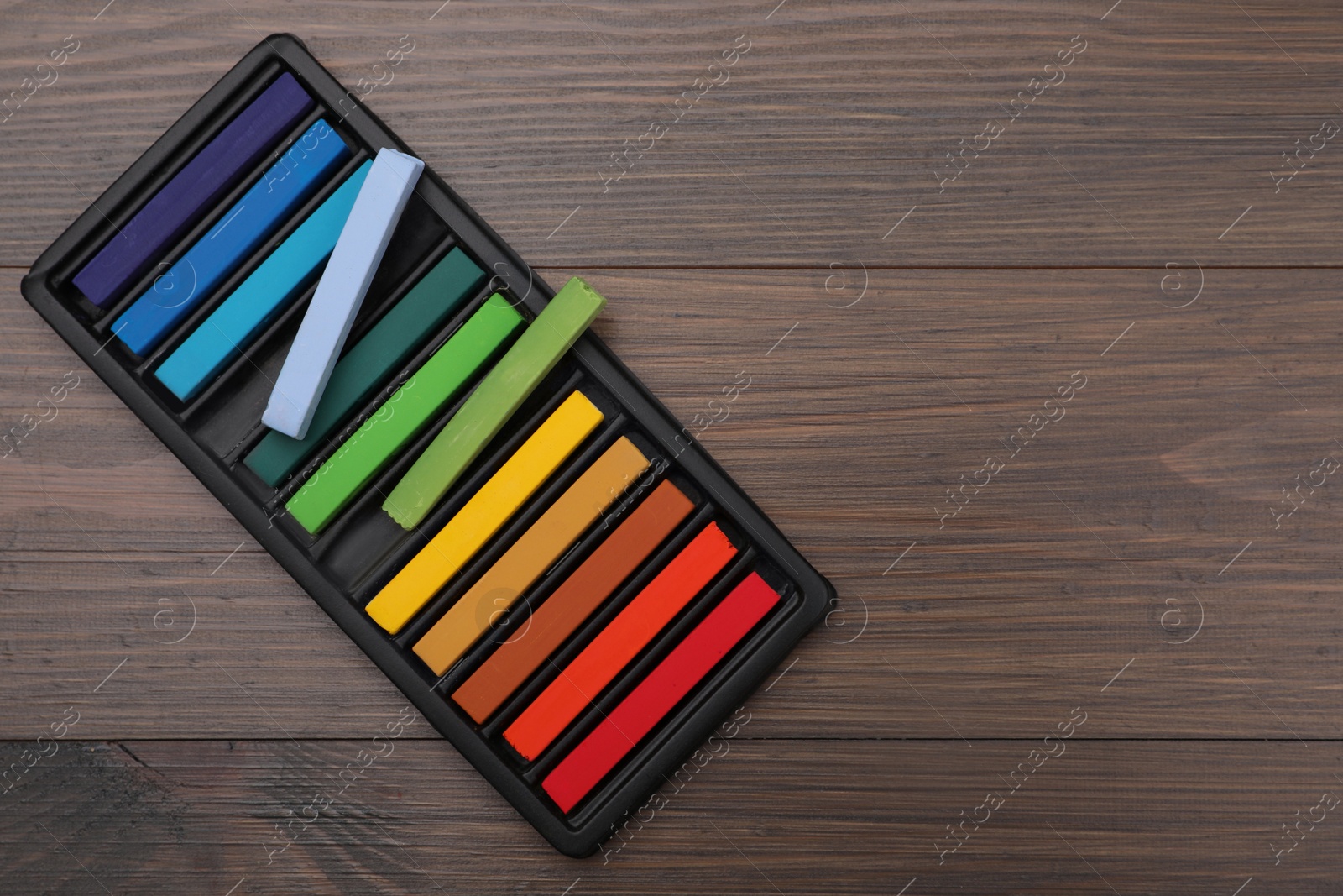 Photo of Colorful pastels in tray on wooden table, top view with space for text. Drawing materials