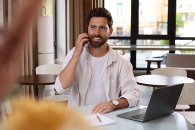 Handsome man talking on phone at table in cafe