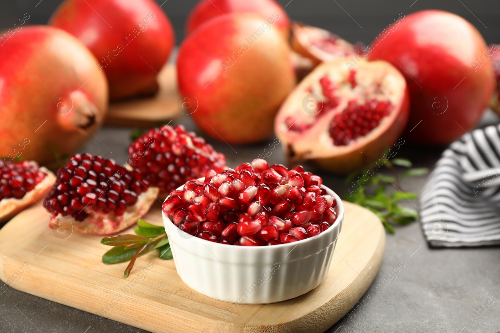 Photo of Delicious ripe pomegranate kernels in bowl on grey table, closeup