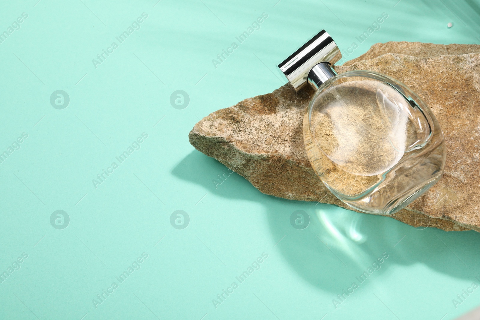 Photo of Bottle of luxury perfume in sunlight and stone on turquoise background, above view. Space for text