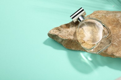 Bottle of luxury perfume in sunlight and stone on turquoise background, above view. Space for text