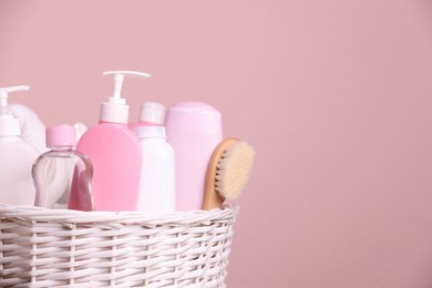 Photo of Baby cosmetic products in wicker basket on pink background, closeup. Space for text