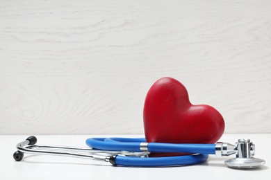 Photo of Medical stethoscope and wooden heart on table. Space for text