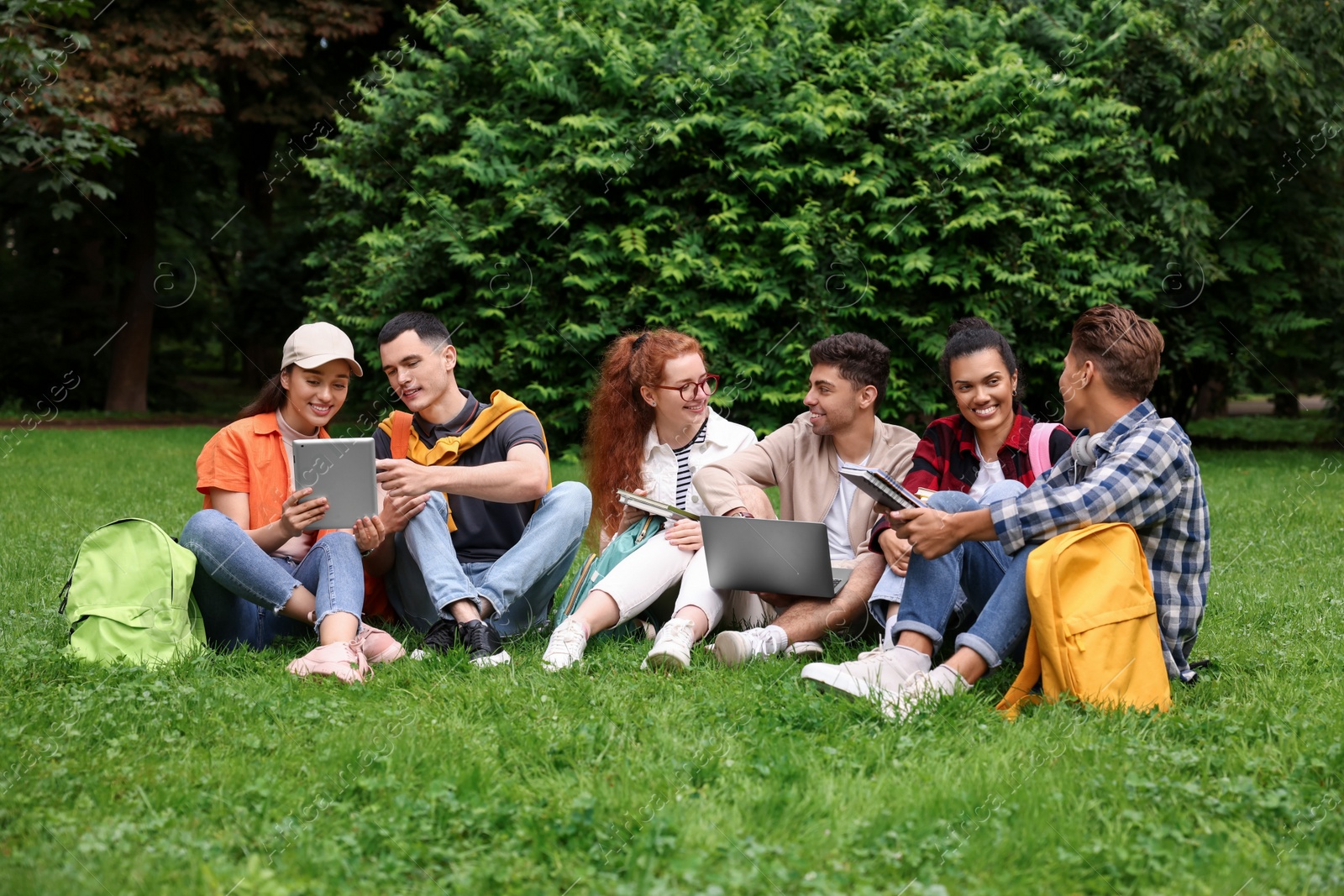 Photo of Group of happy young students learning together on green grass in park