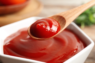 Photo of Spoon and bowl with homemade tomato sauce on table, closeup