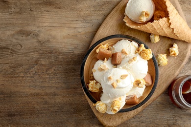 Plate of delicious ice cream with caramel candies and popcorn on wooden table, flat lay. Space for text