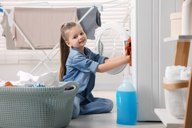 Photo of Little girl putting dirty clothes into washing machine in bathroom