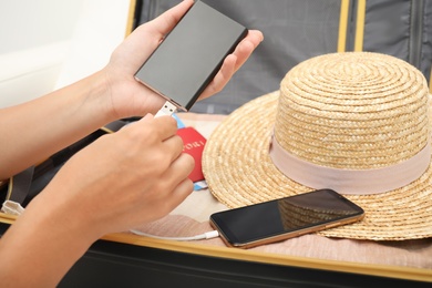 Photo of Woman charging smartphone with power bank near packed suitcase indoors, closeup