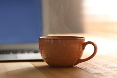 Photo of Delicious coffee and laptop on wooden table. Good morning