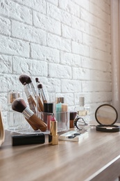 Organizer with cosmetic products for makeup on table near brick wall