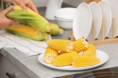 Photo of Plate with ripe corn cobs and blurred woman on background