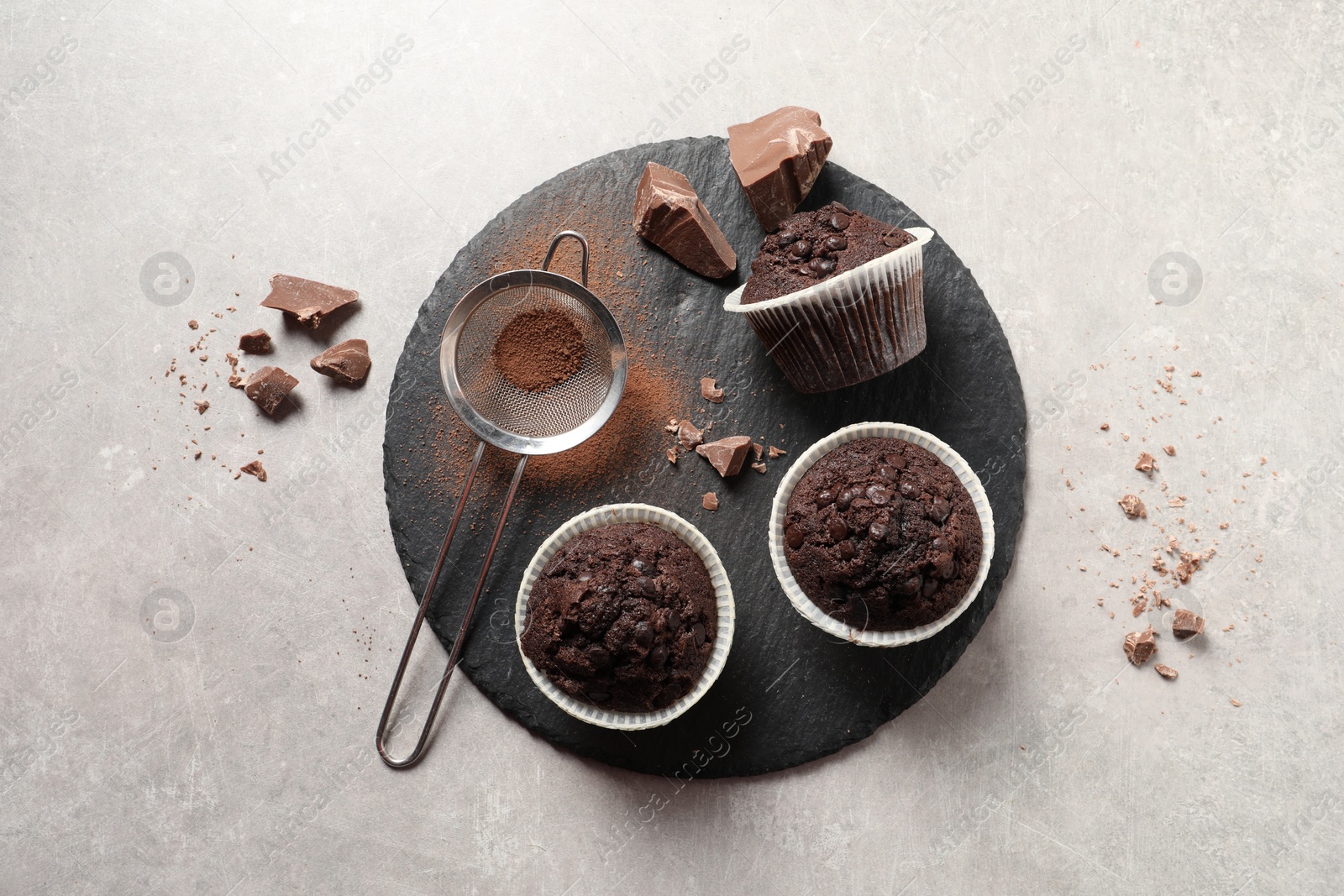 Photo of Delicious chocolate muffins and sieve with cocoa powder on light table, top view