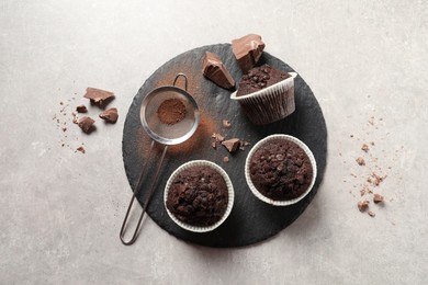 Photo of Delicious chocolate muffins and sieve with cocoa powder on light table, top view