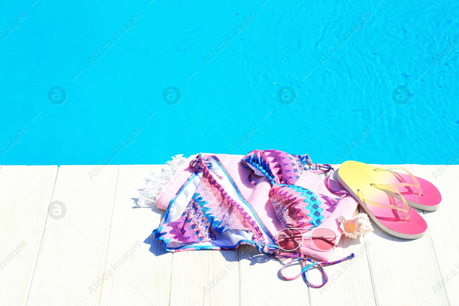 Photo of Beach accessories on wooden deck near swimming pool. Space for text