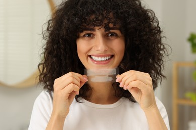 Photo of Young woman holding teeth whitening strips in bathroom