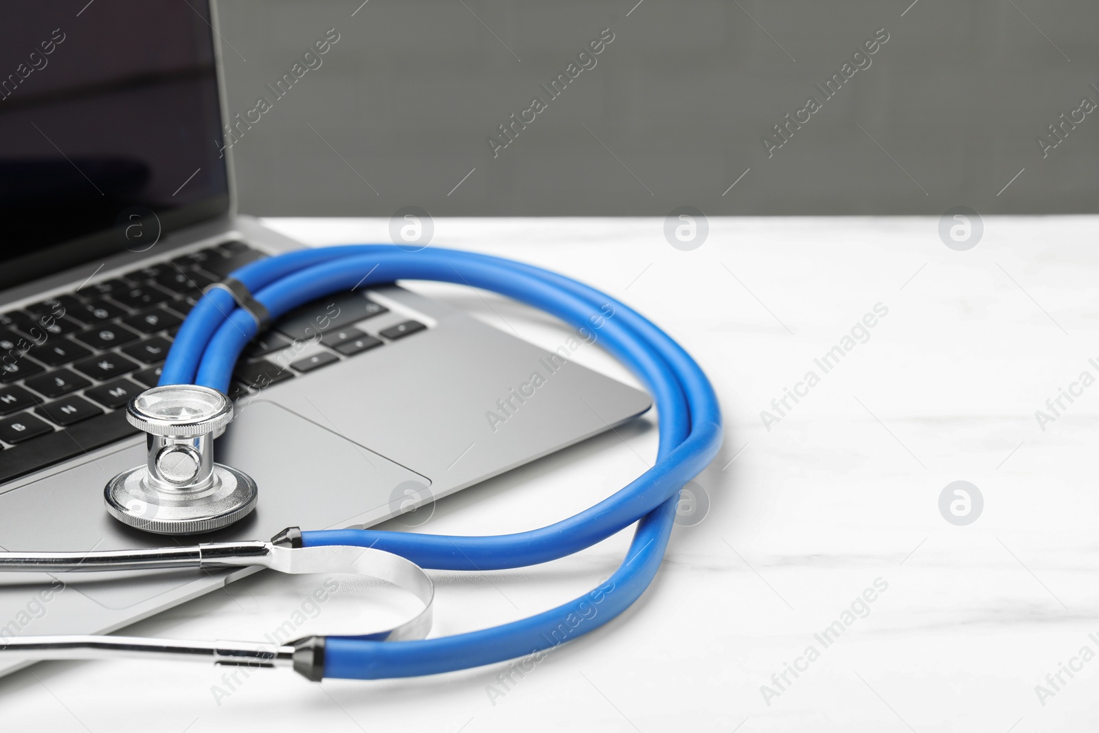 Photo of Stethoscope and modern laptop on white table. Space for text