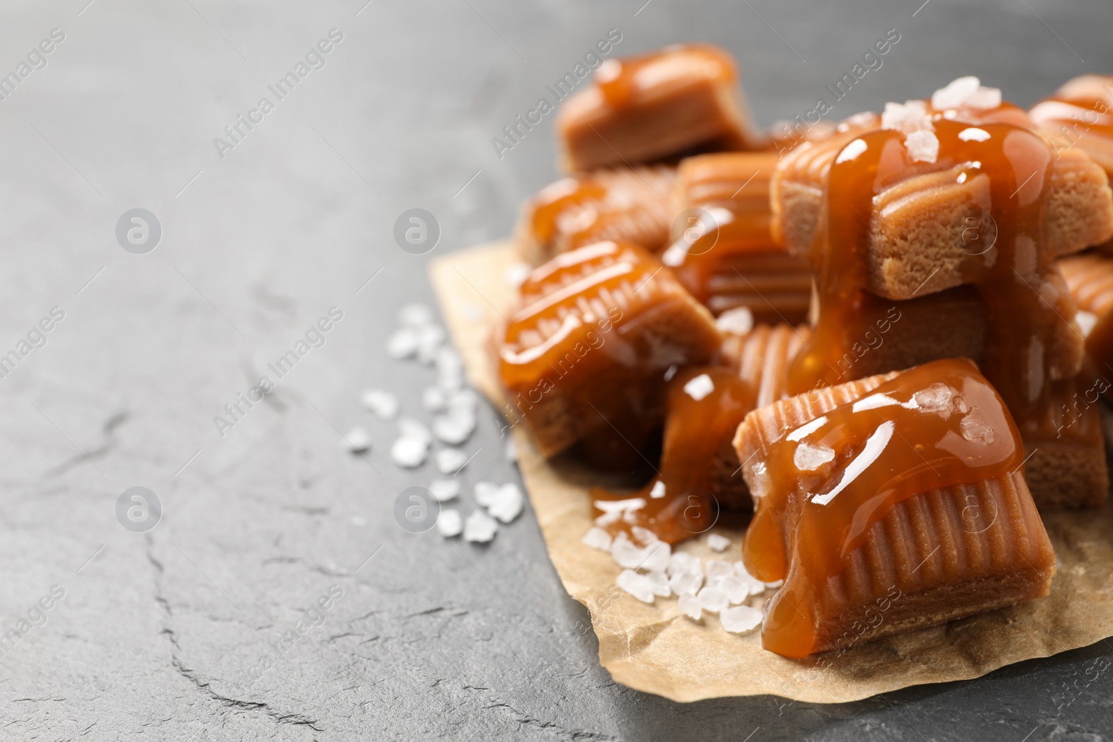 Photo of Tasty caramel candies with sauce and sea salt on grey table, closeup. Space for text