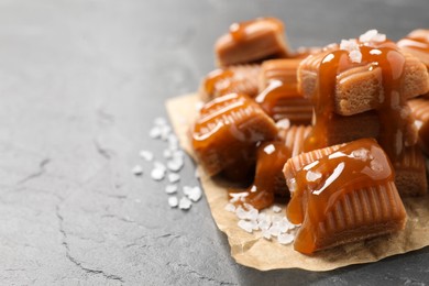 Tasty caramel candies with sauce and sea salt on grey table, closeup. Space for text