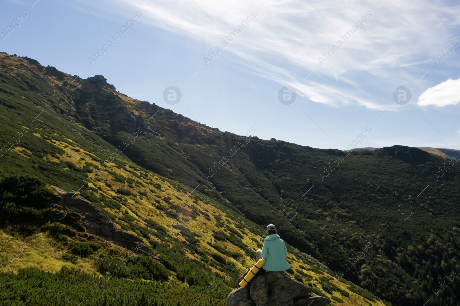 Image of Woman with sleeping mat on rocky cliff in mountains, back view